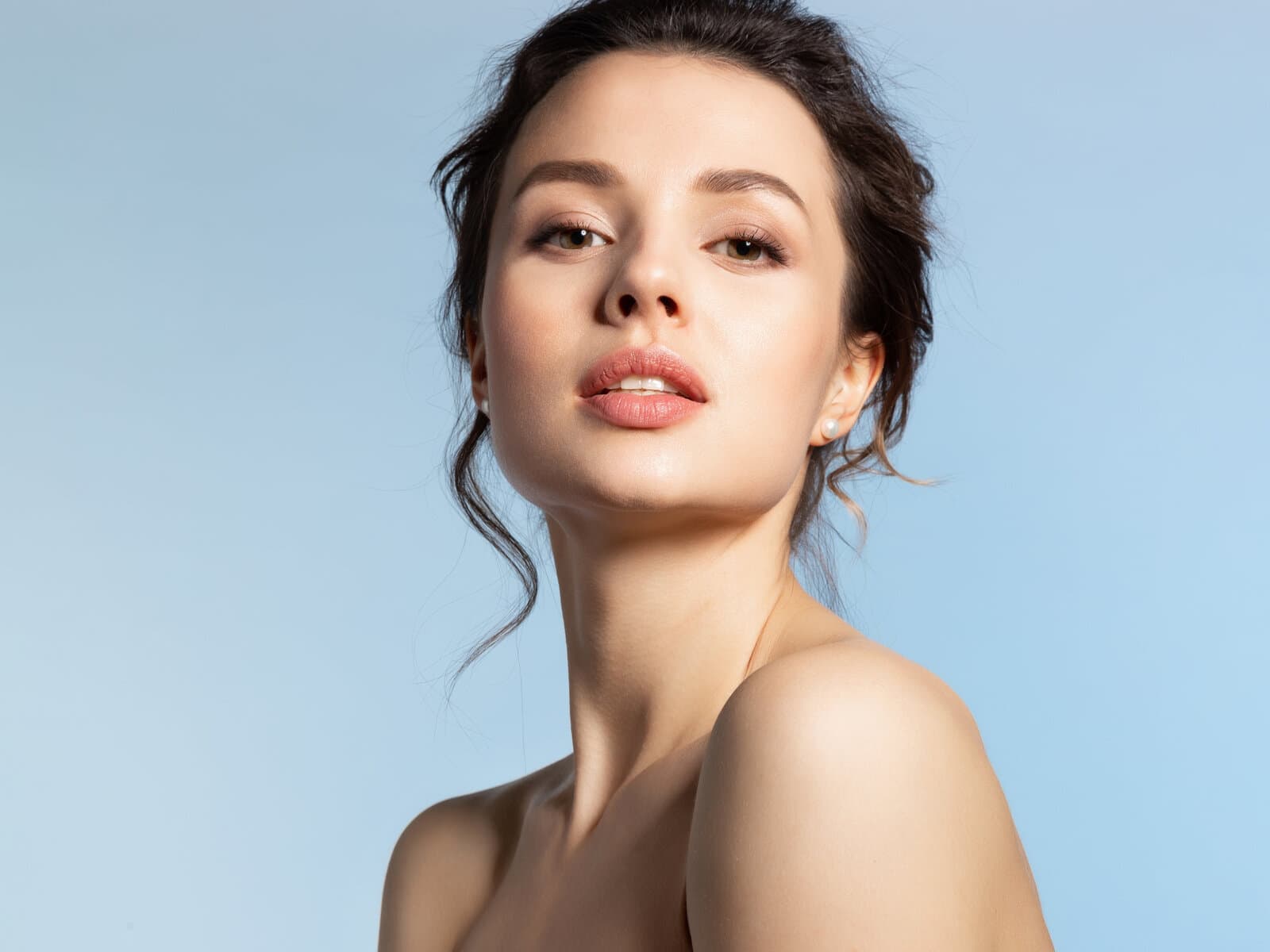 A woman turned to one side against a pale blue ground, the skin of her cheek and neck an even tone