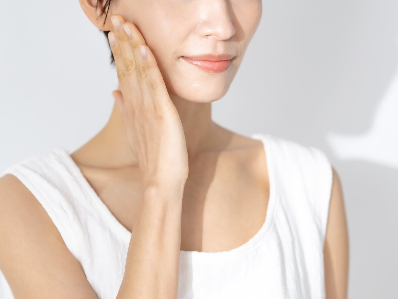 A woman in a white vest with one hand raised to her cheek, shoulder and upper arm bare and unmarked
