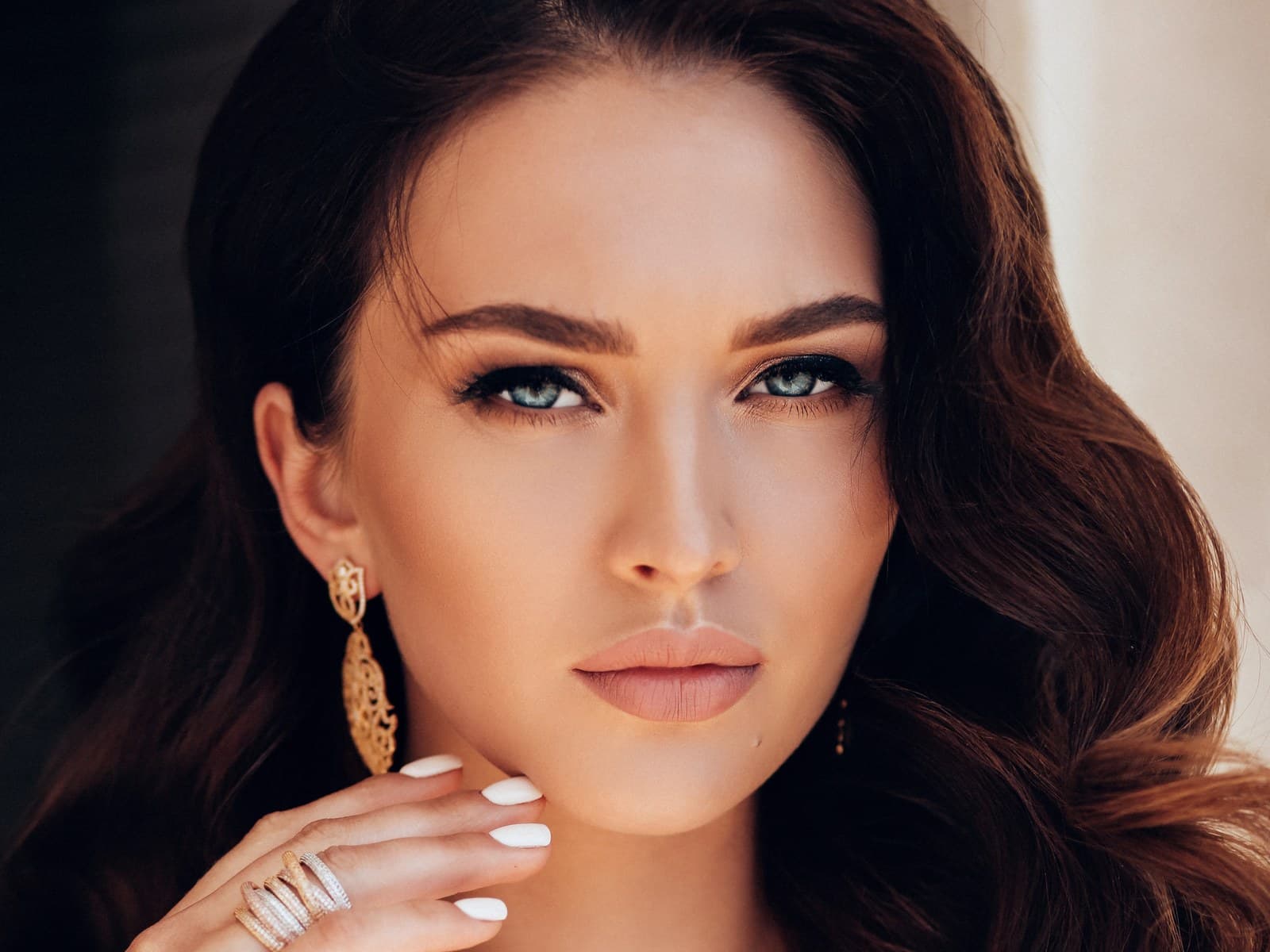 A woman looking directly at the camera, dark wavy hair over one shoulder, one hand raised to her jaw