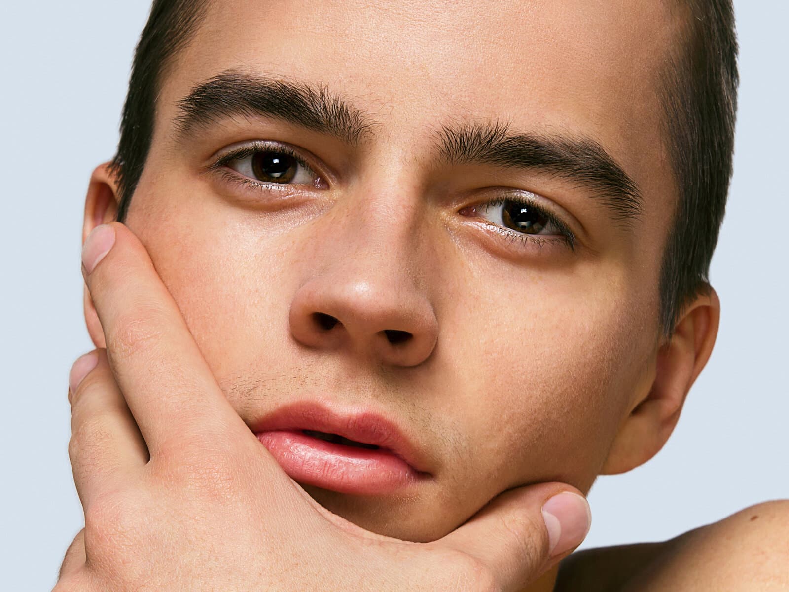 A young man's face at close range, his chin resting on one hand, skin clear and evenly lit