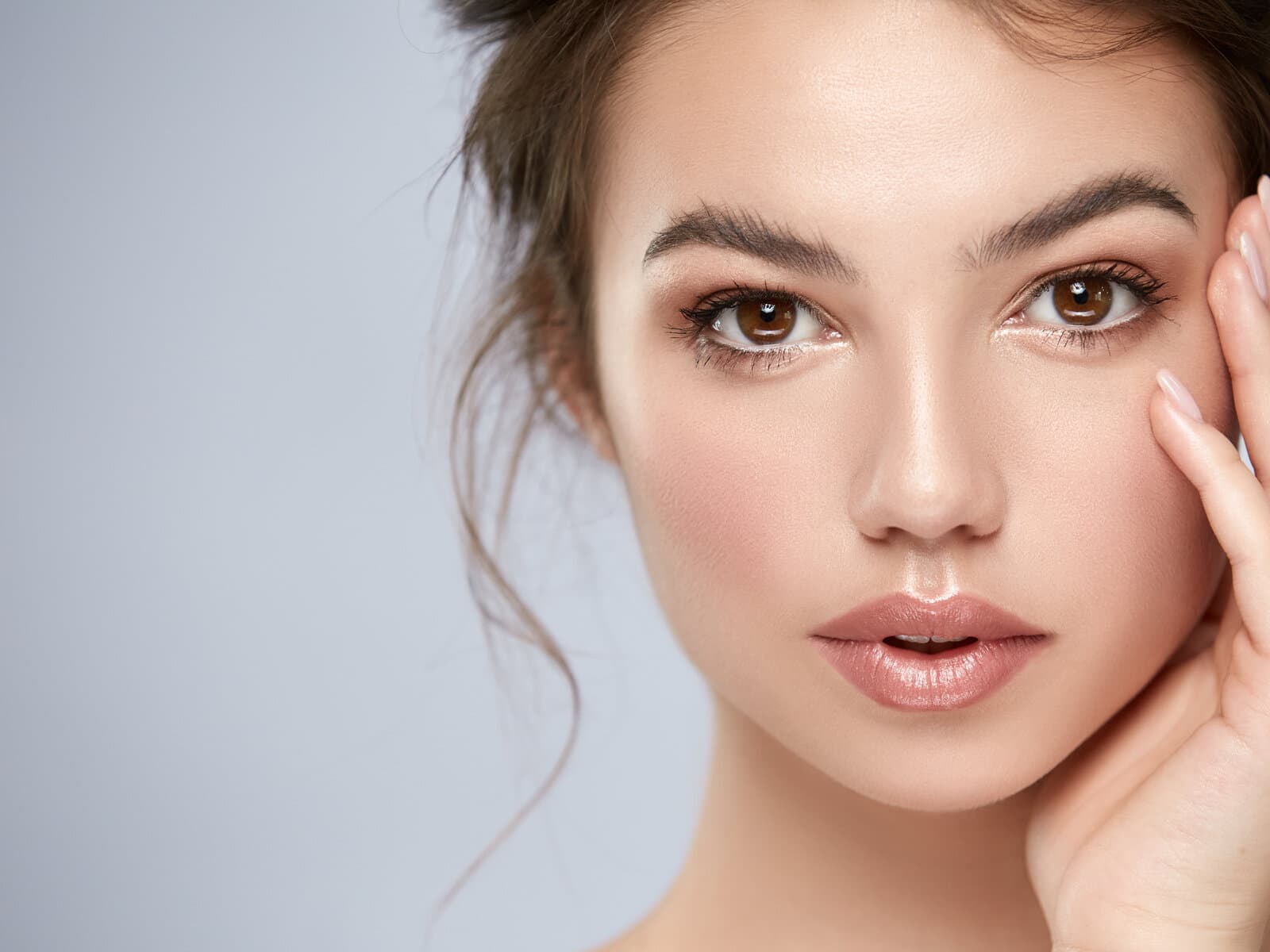 A woman's face lit evenly from the front, one hand at her cheek, the skin a single unbroken tone